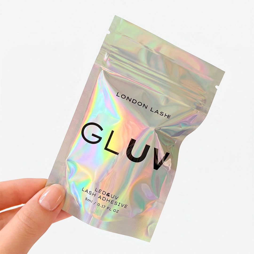 A hand holding the iridescent holographic resealable pouch packaging for London Lash GLUV LED & UV Lash Adhesive.