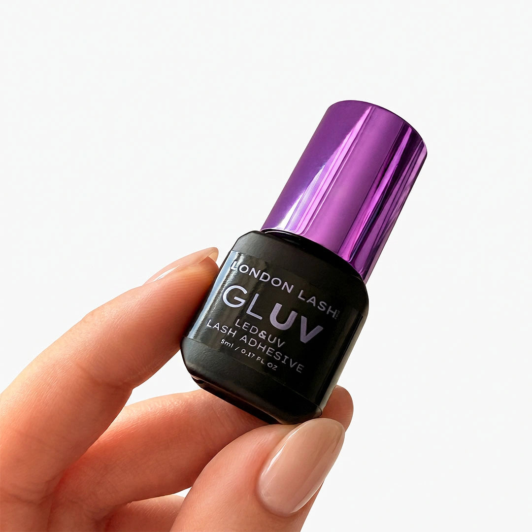 Close-up of a manicured hand holding the 5ml bottle of London Lash GLUV Lash Adhesive with a shiny purple lid.